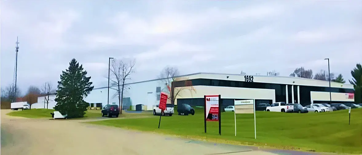 広い敷地内にある白い工業系の建物。正面に駐車場があり、数台の車が停まっている。建物には「1652」の番号が表示されている。物流倉庫や海外拠点施設の外観と見られる。