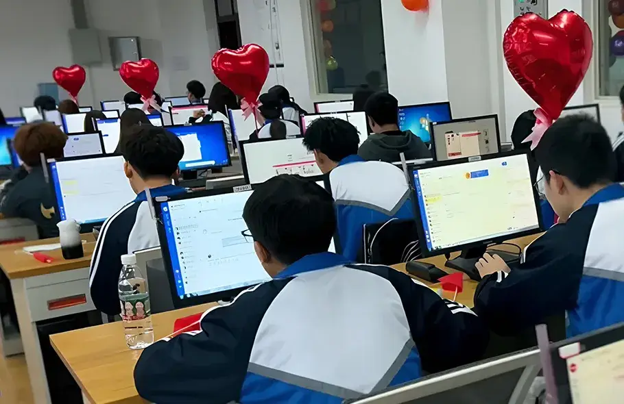 Room resembling a classroom where several people are working at computers, with red heart-shaped balloons placed on the desks, creating a bright and cheerful atmosphere.