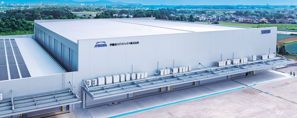 伊藤忠ロジスティクス株式会社の物流センター外観。近代的なグレーの建物で、社名とロゴが壁面に掲げられている。晴天の下、整備中の敷地とフェンスが写っている。