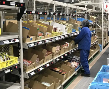 Worker sorting food products on shelves inside a frozen warehouse, with multiple boxes organized for an active picking system.