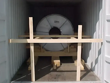 コンテナ内に木枠でしっかり固定された金属コイル。輸送中の揺れを防ぐため、木製の支持構造で安全に梱包されている様子。