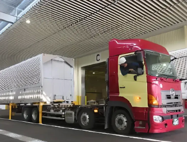Red truck delivering large cargo at a factory loading entrance.