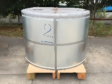 屋外で撮影された大型の金属コイル。銀色に輝く表面を帯鉄で固定し、木製パレットの上に載せられている。工場敷地内の出荷や保管中の様子を示している。