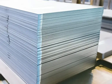 工場内に積み重ねられた多数の金属板。光沢のある表面が整然と並び、加工や出荷前の保管状態を示している。